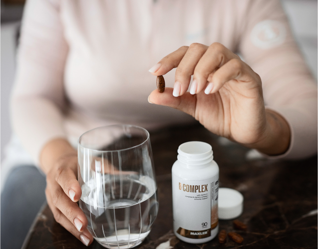 A photo of a woman takin a B-Complex tablet.