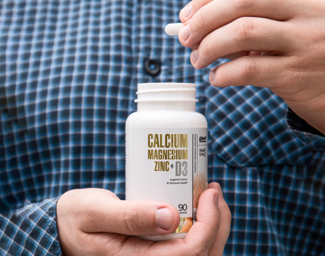 A photo of hands holding Calcium Magnesium Zinc+D3 bottle and a tablet.