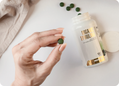 A photo of a hand holding one tablet of Organic Spirulina.